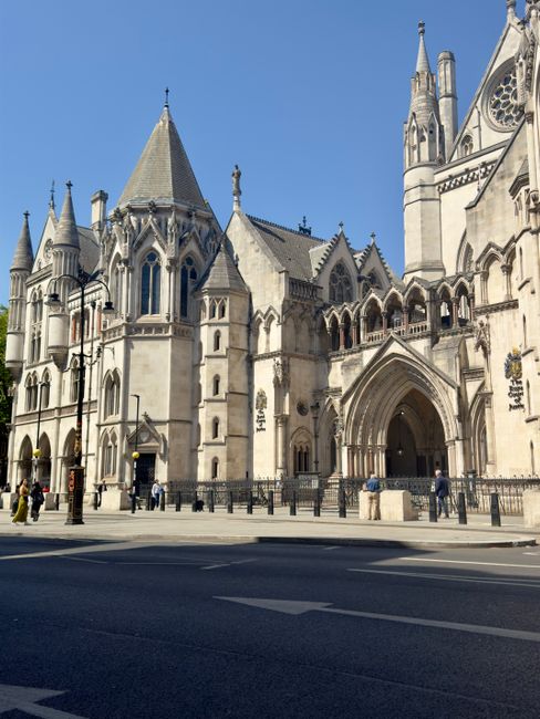 No objects related to house removals, furniture, boxes, or moving equipment are visible in this image. The photo depicts a large historic Gothic-style church or cathedral with detailed stone architecture, pointed arches, and tall spires, situated on a city street. In the foreground, the paved road and sidewalk are visible, with a few pedestrians walking nearby. The sky above is clear and blue, and street lamps are positioned along the pavement. There are no signs of moving or relocation activities, furniture, or packing materials present in this image. The setting appears to be an urban environment, but it does not showcase any house removals or transportation services from Man with Van Earls Court.